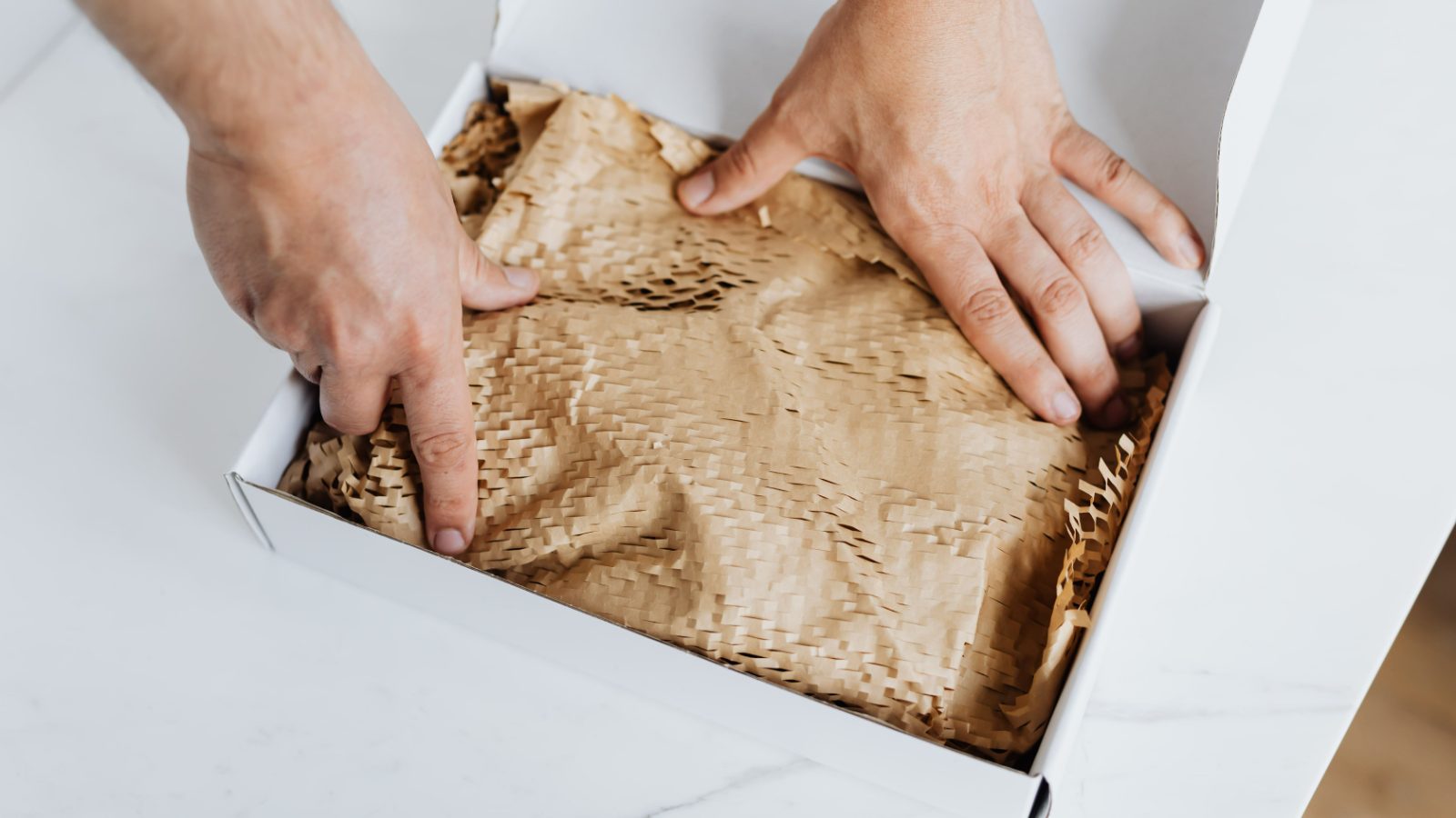 Hände packen einen Karton mit Papierpolster für den Versand